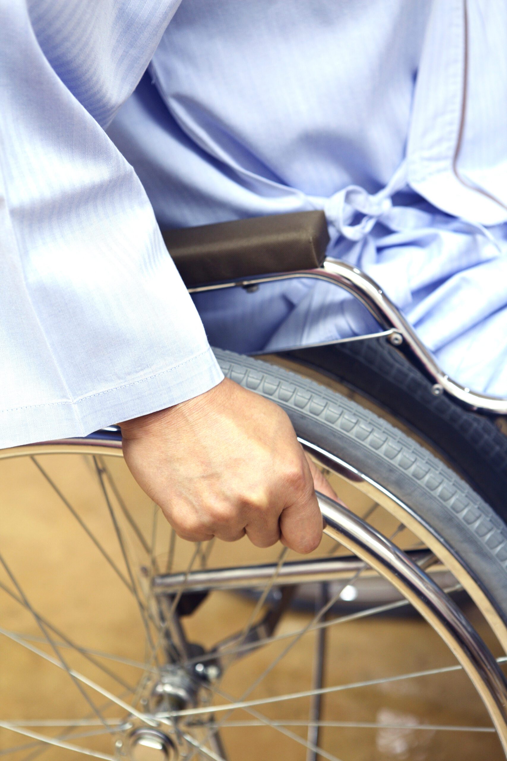 Close-up of a man in a blue robe, hand pedaling the wheel of a wheelchair.