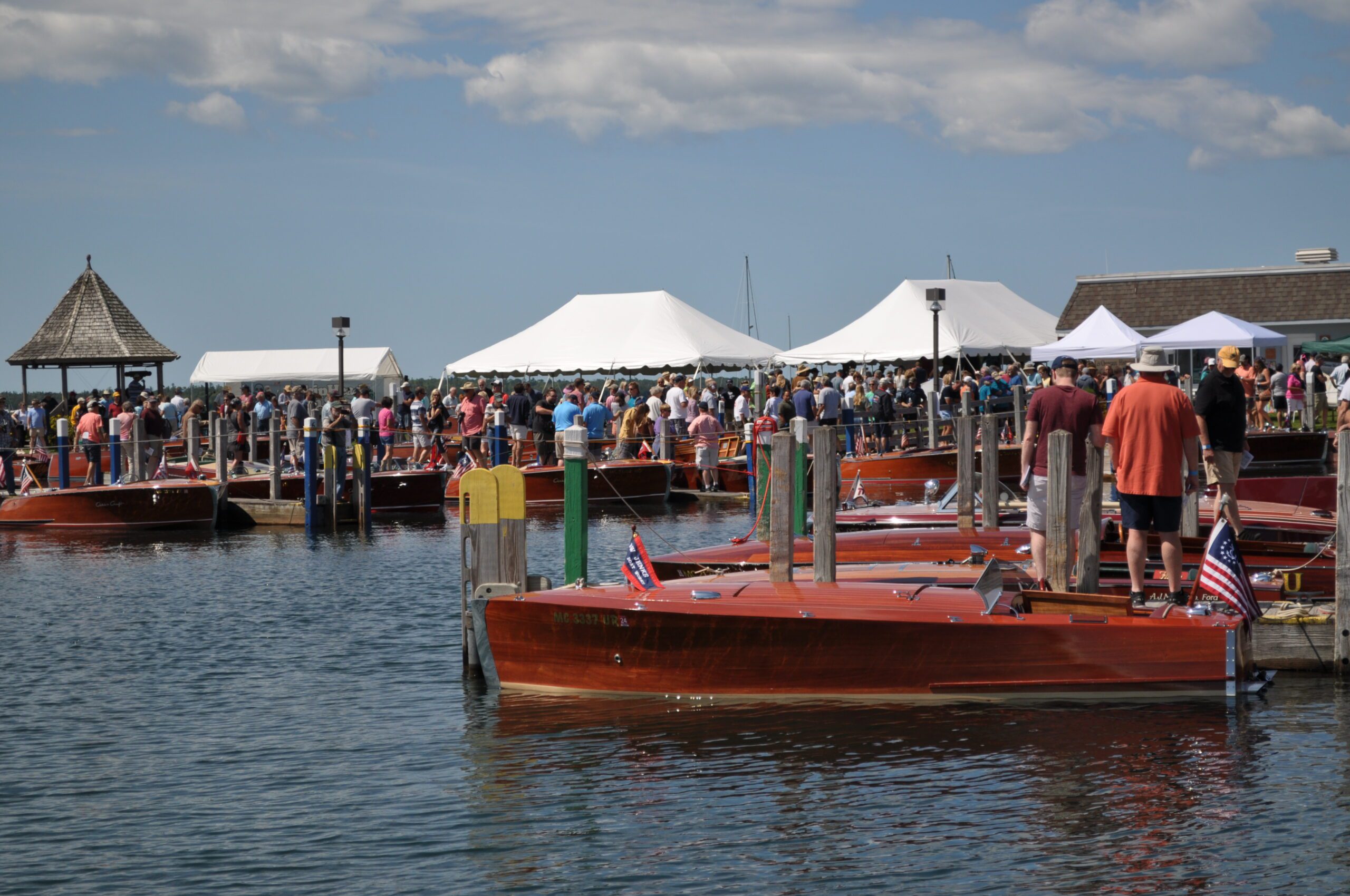 Crowds gather on a dock at a boat show, viewing classic wooden boats.