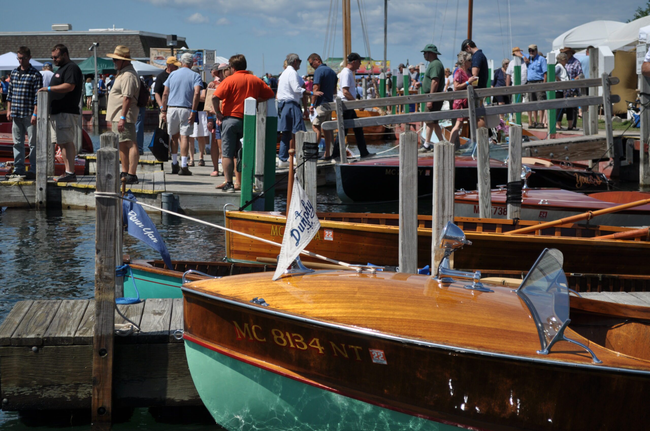 People walking on a dock at a boat show, viewing classic wooden boats.