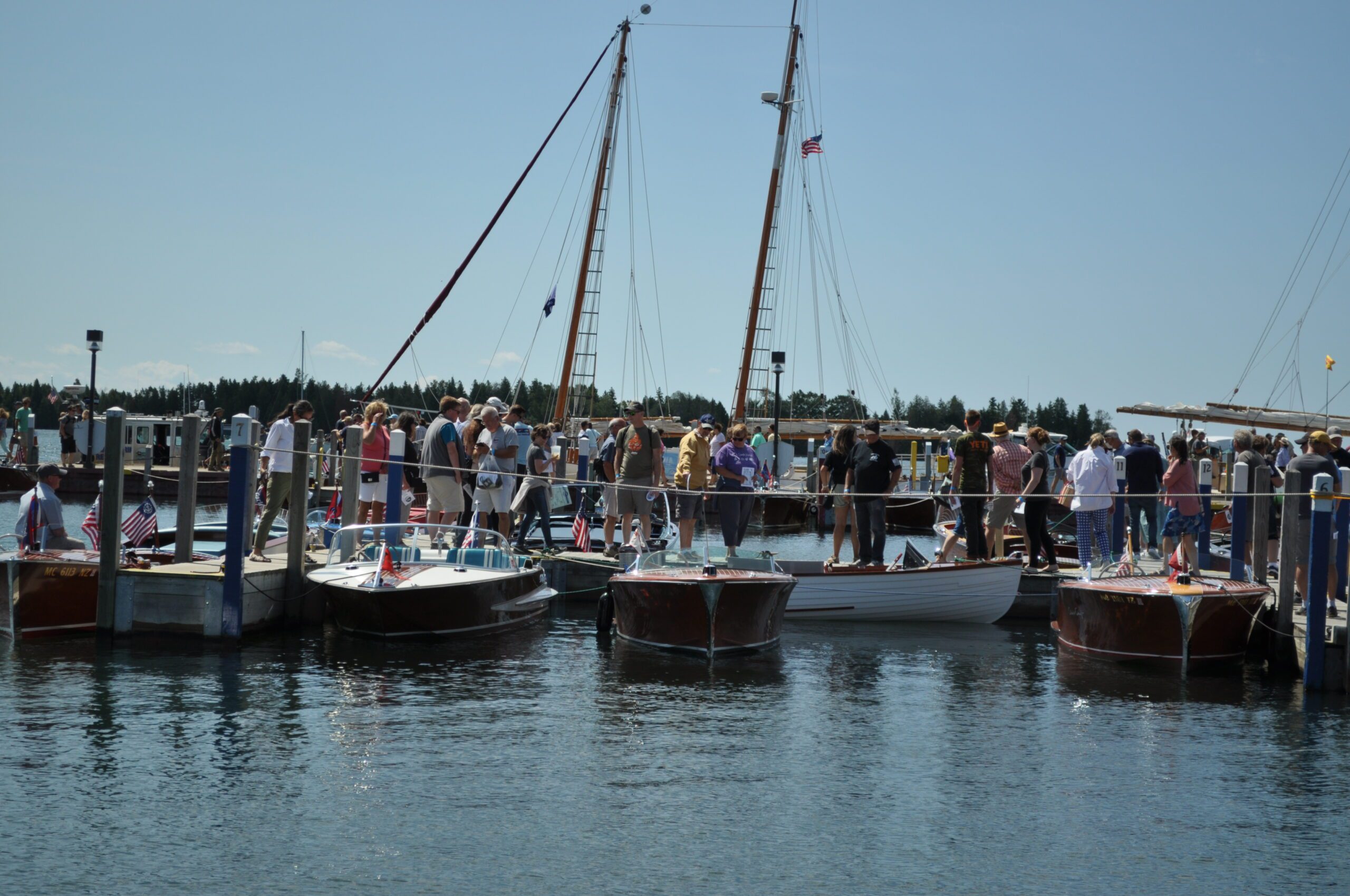 People walking on a dock at a boat show, viewing a collection of classic wooden boats.