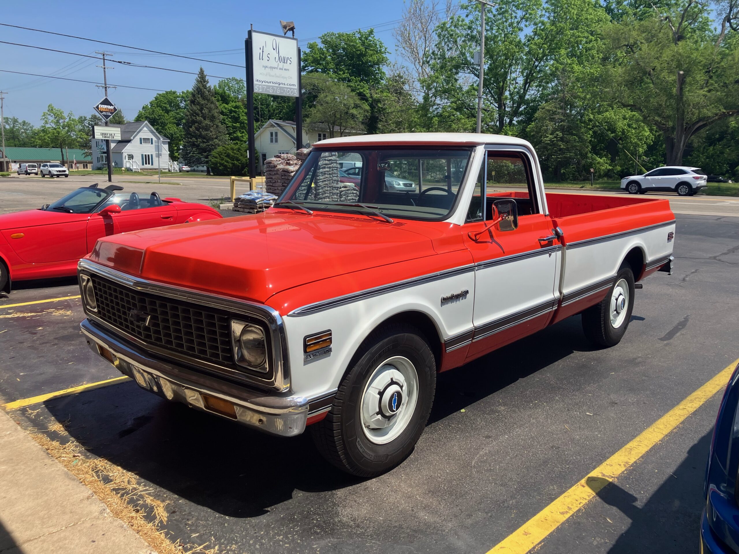 A classic red and white Chevrolet pickup truck parked in a lot on a sunny day.