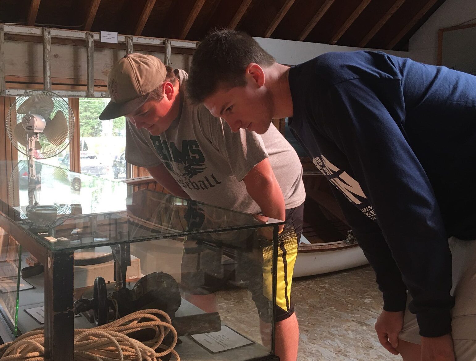 Two men leaning over a glass display case, closely examining maritime artifacts inside a museum.