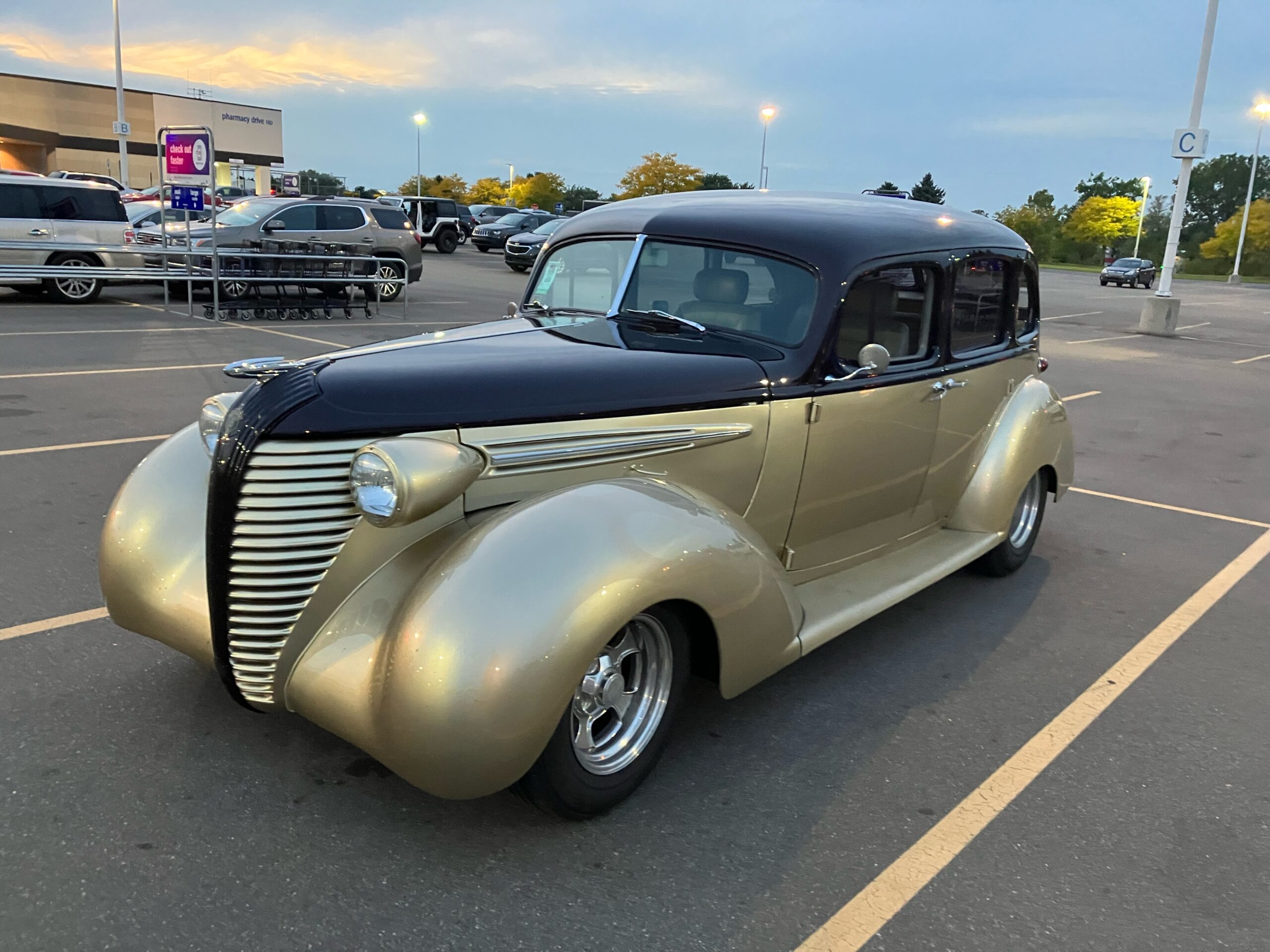 A gold and black vintage car with a sleek design parked in a parking lot during twilight.