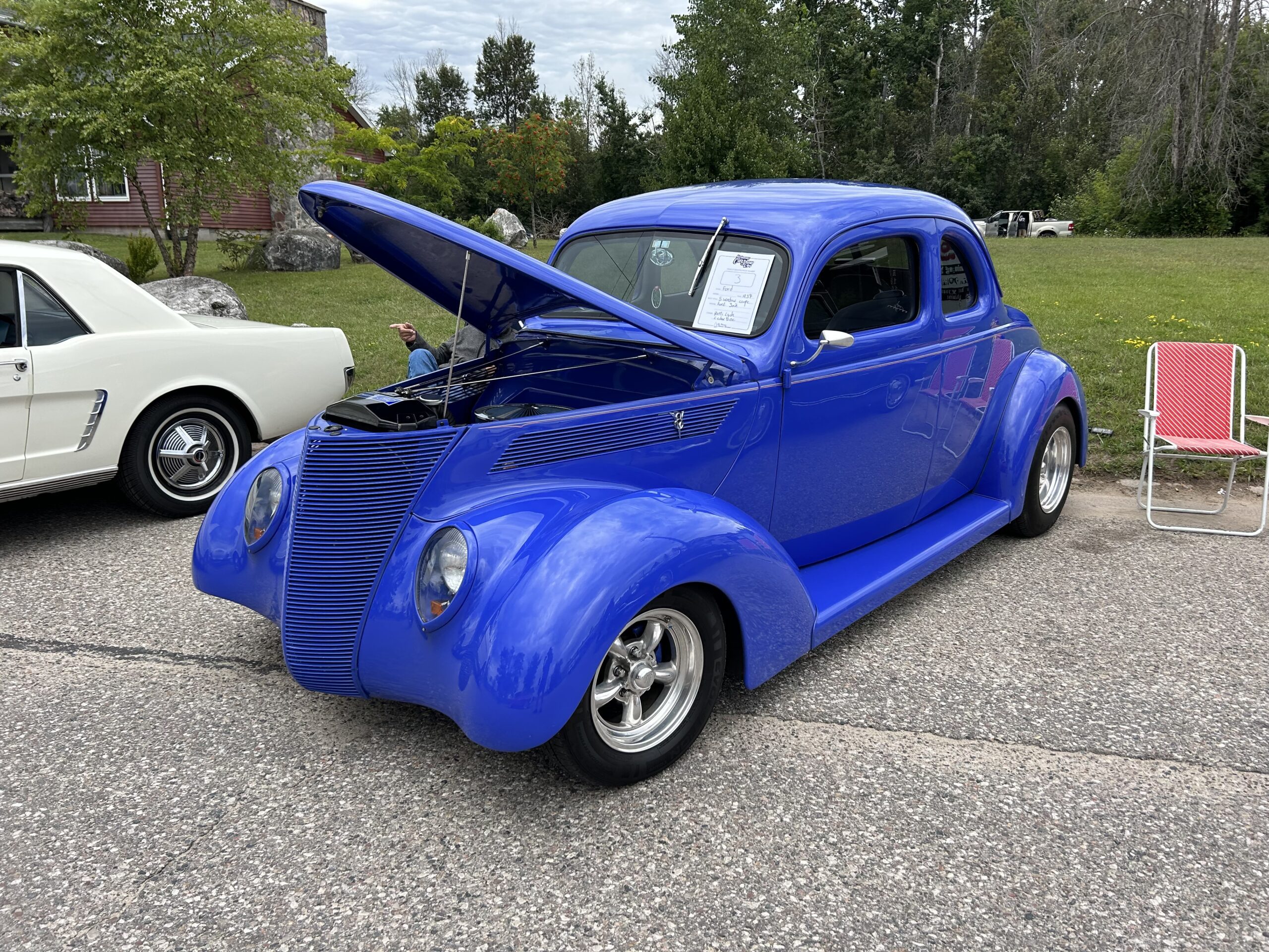 A bright blue vintage car with the hood open, displayed at an outdoor car show.