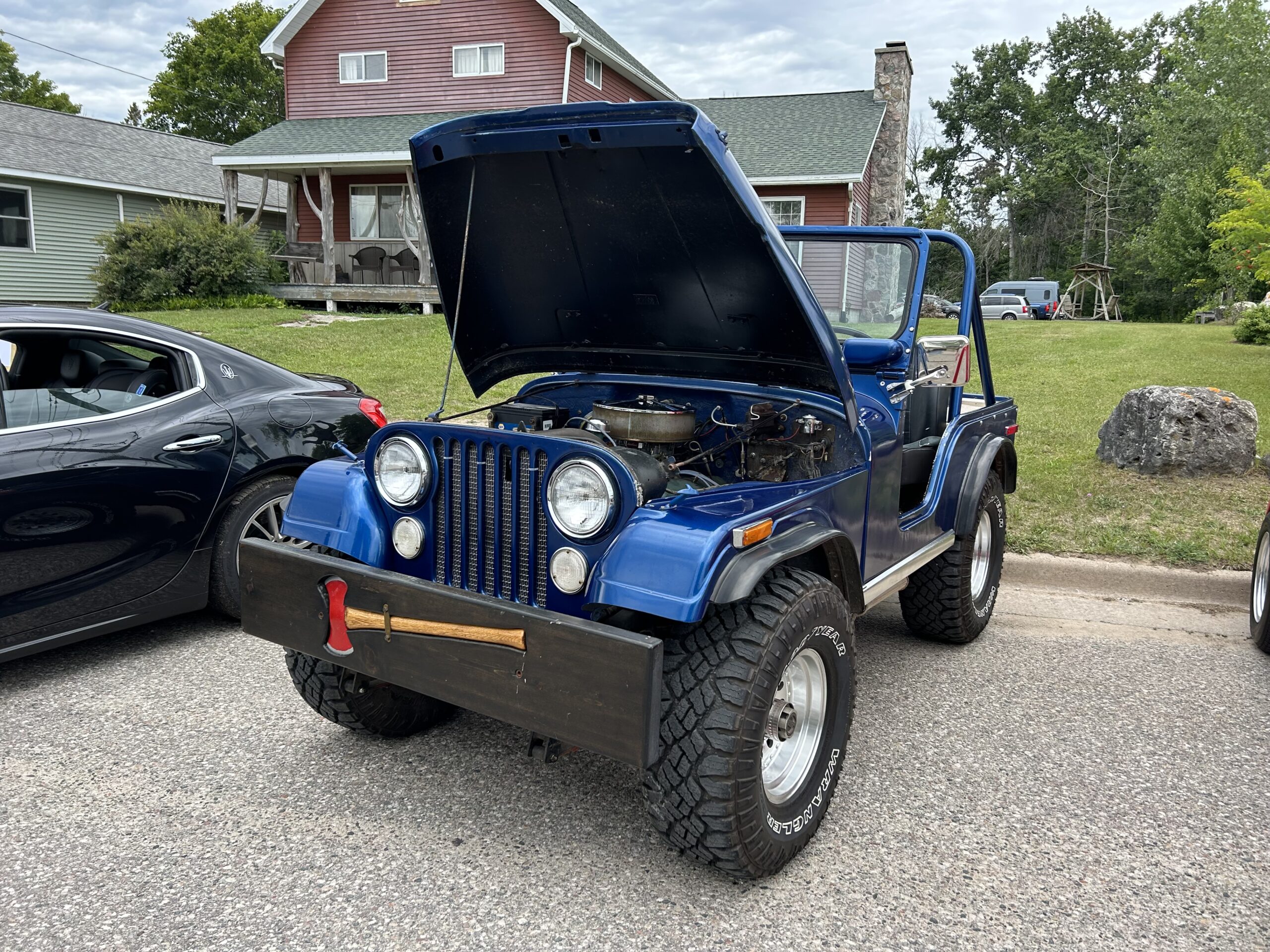 A blue Jeep with the hood open, displaying its engine at an outdoor car show.