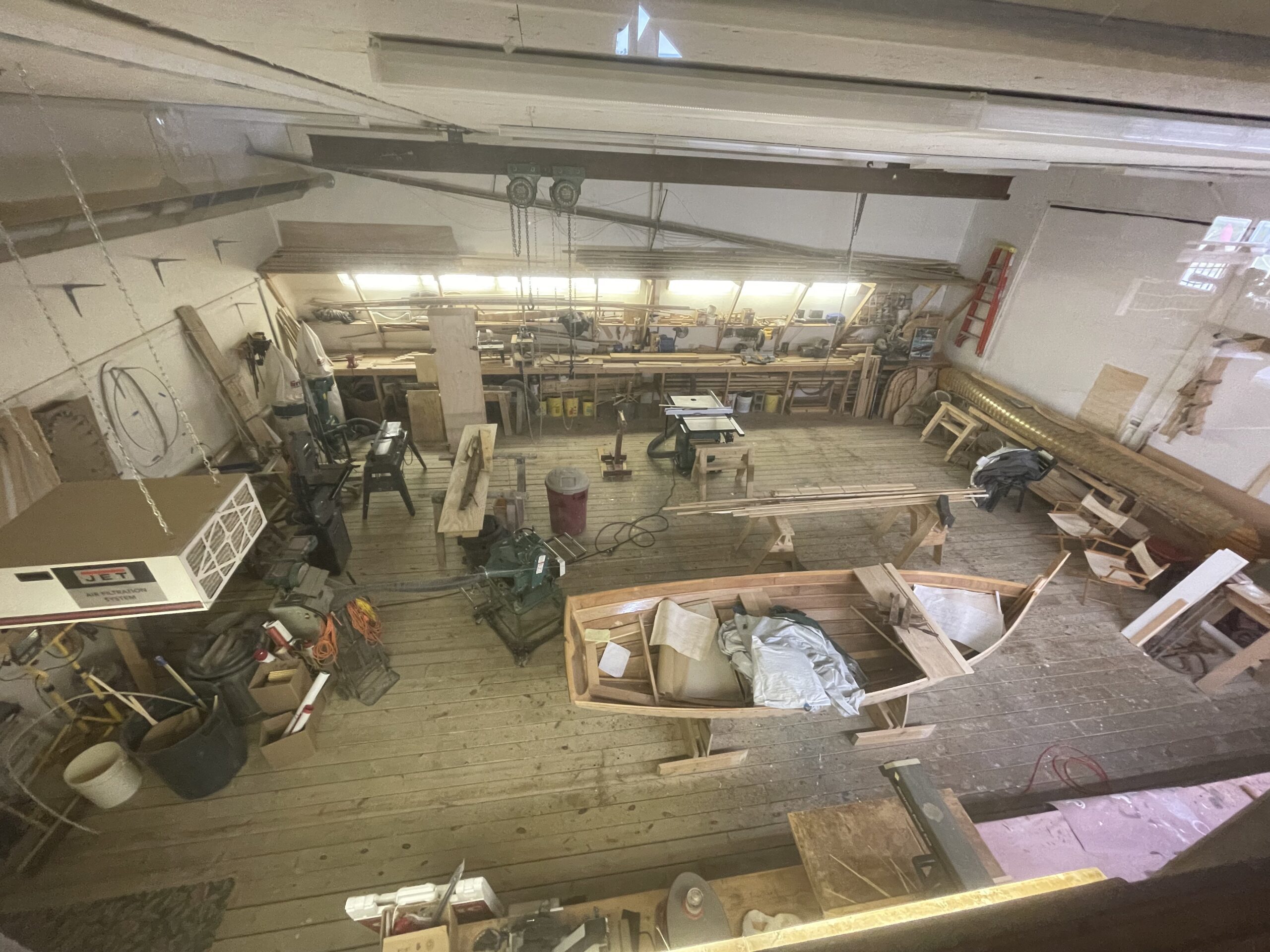 A large woodworking shop with various tools, benches, and wooden projects in progress, including a partially built boat on the floor.