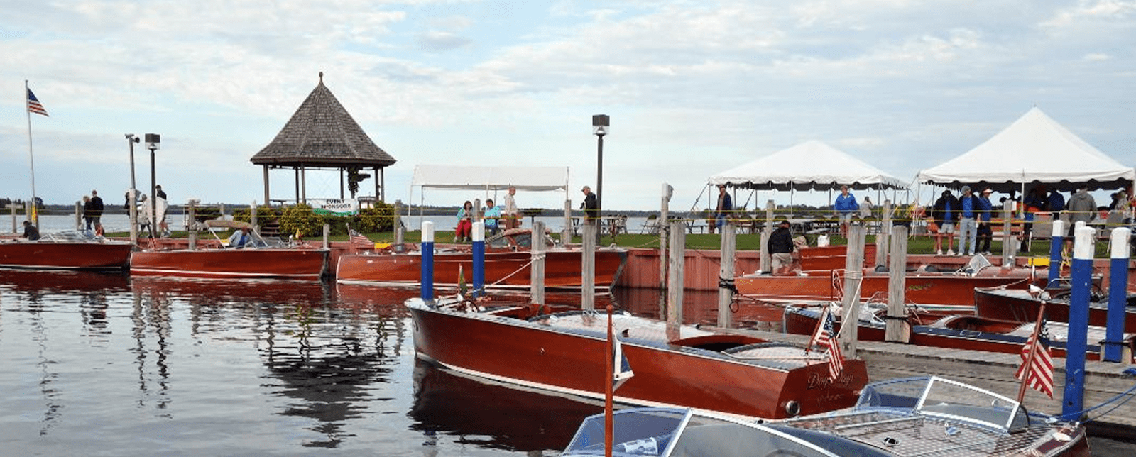 Vintage wooden boats docked at a marina with people mingling around.