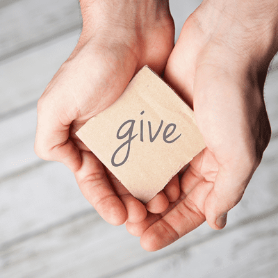 A pair of hands holding a small cardboard piece with the word "give" written on it in lowercase letters.