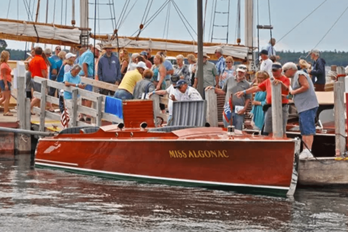 Crowd observing the vintage boat "Miss Algonac" at a wooden boat show at the dock.