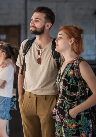 A young couple, with the man wearing a beige shirt and the woman in a patterned dress, attentively viewing an exhibit in a museum.